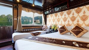 A hotel room with a large bed, a window with curtains, and a view of a boat on the water. - Golden Star Cruise (Tuan Chau)