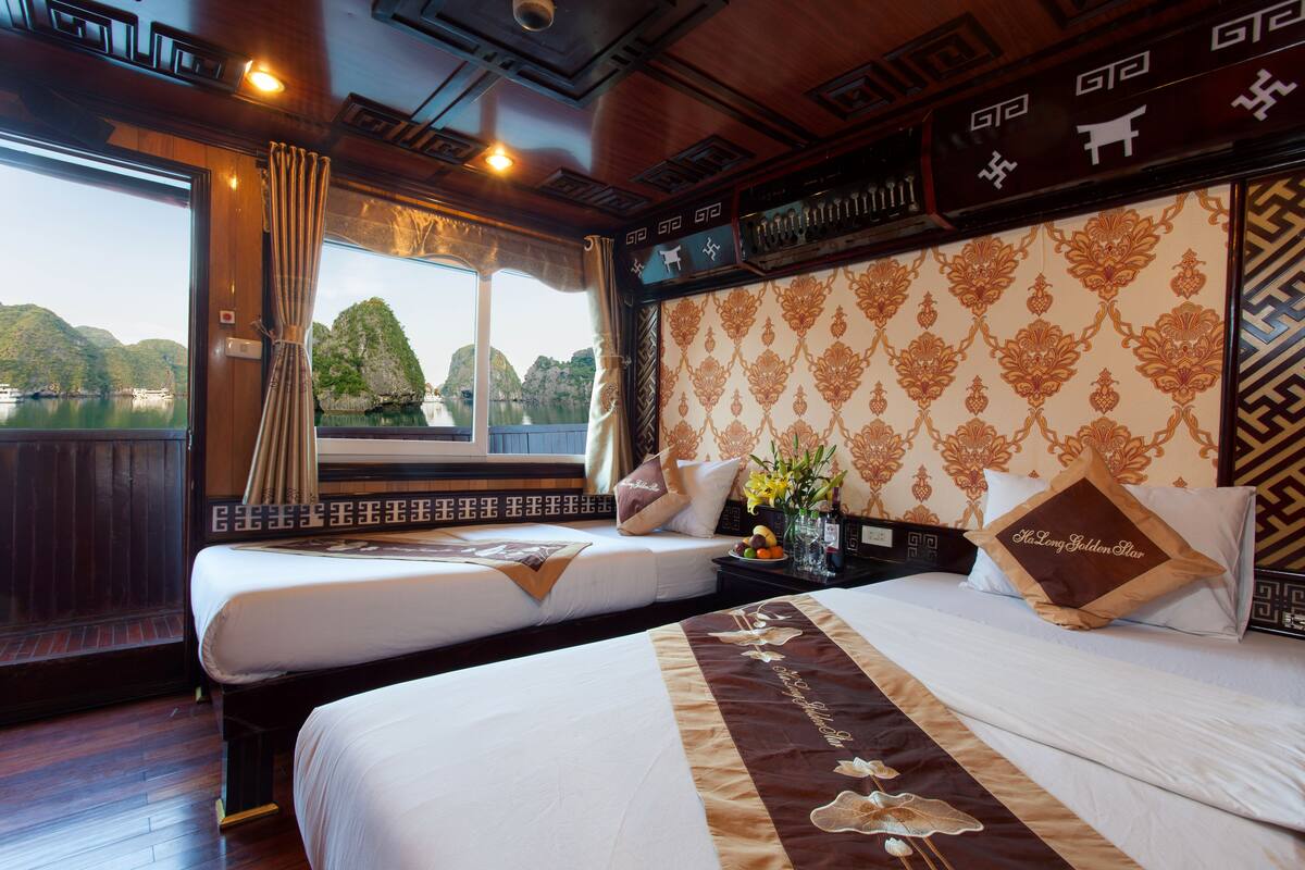 A hotel room with two beds, a large window with curtains, a decorative headboard, and a nightstand with a vase of flowers.