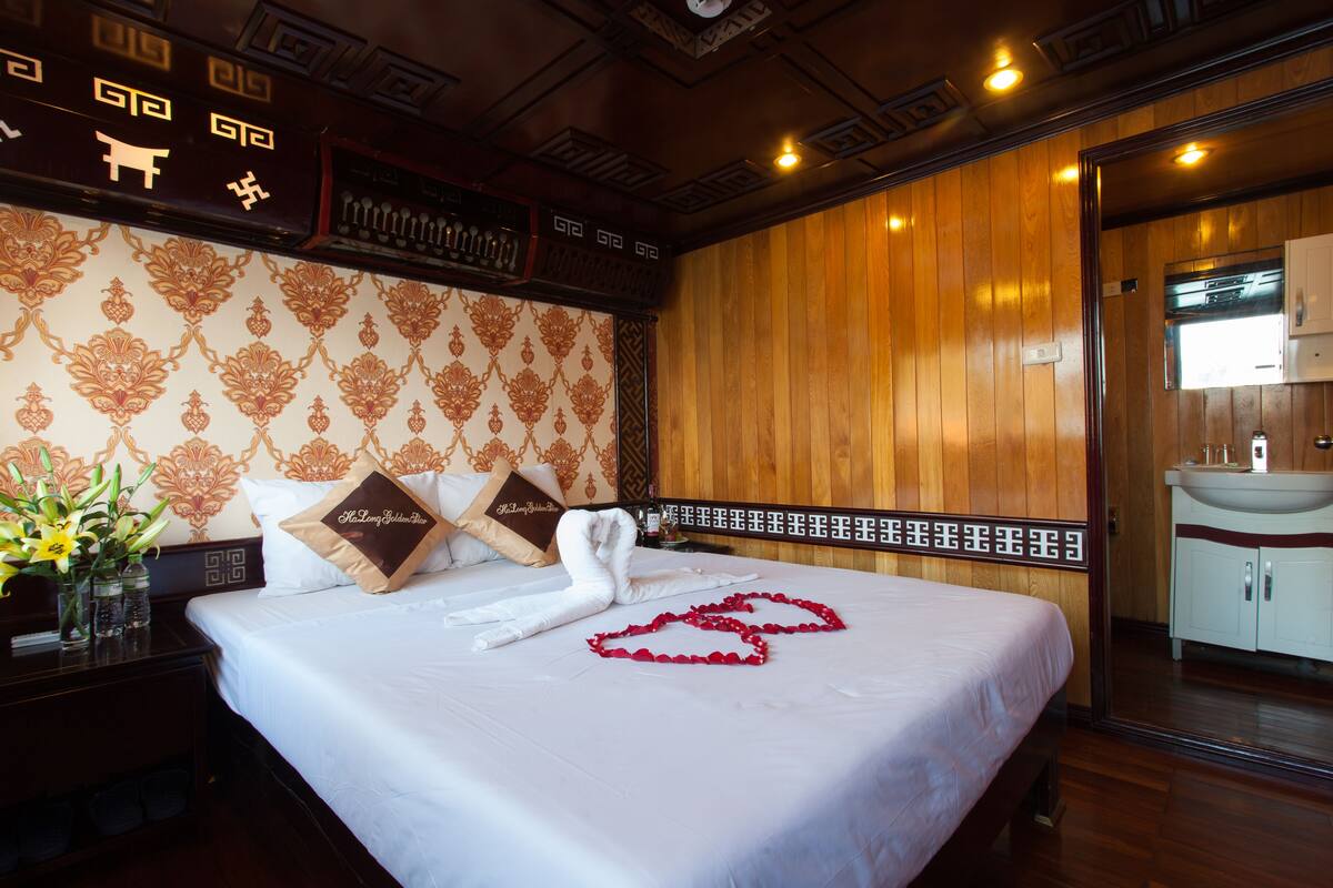 A hotel room with a neatly made bed, a wooden headboard, and a bathroom visible through an open door.