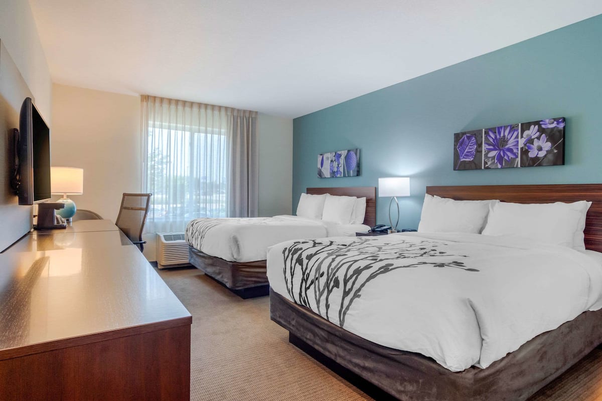 A hotel room with two beds, a desk, a flat-screen TV, and artwork on the walls.