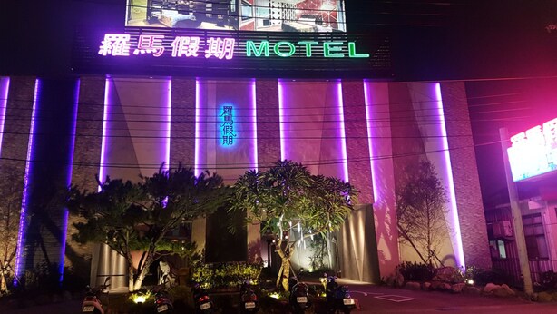 A motel with a neon sign, a large entrance, and several parked motorcycles. - Roman Vacation Motel (Taichung)