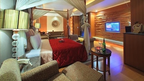 A hotel room with a four-poster bed, a television, a small table with a candle, and a seating area with patterned sofas. - Roman Vacation Motel (Taichung)