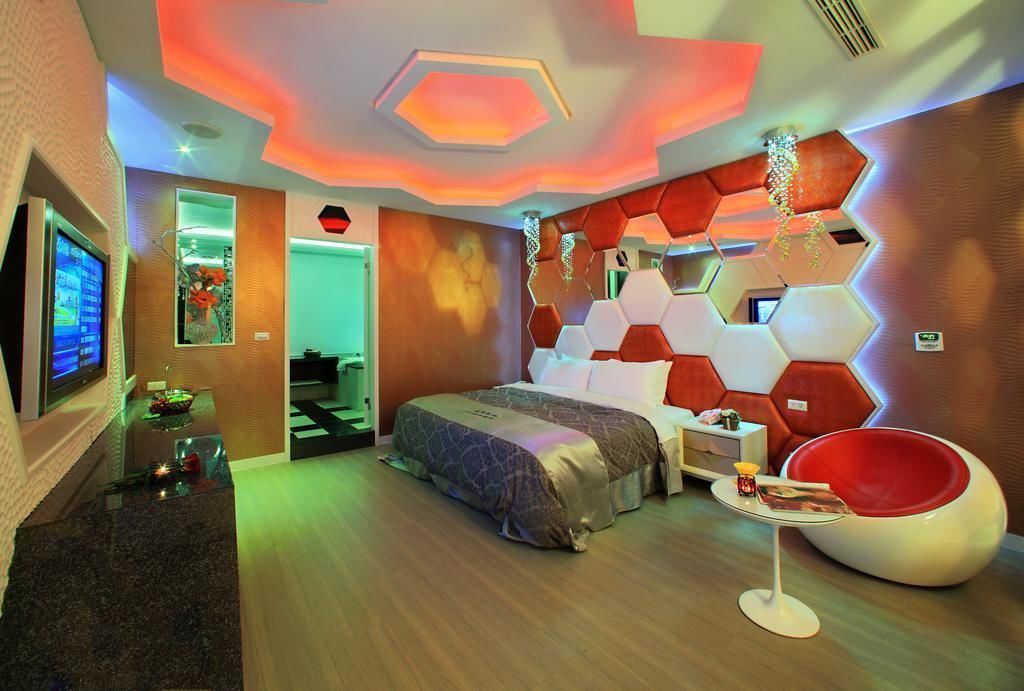 Une chambre d’hôtel moderne avec un grand lit, un fauteuil rouge et un téléviseur placé sur le mur de gauche.