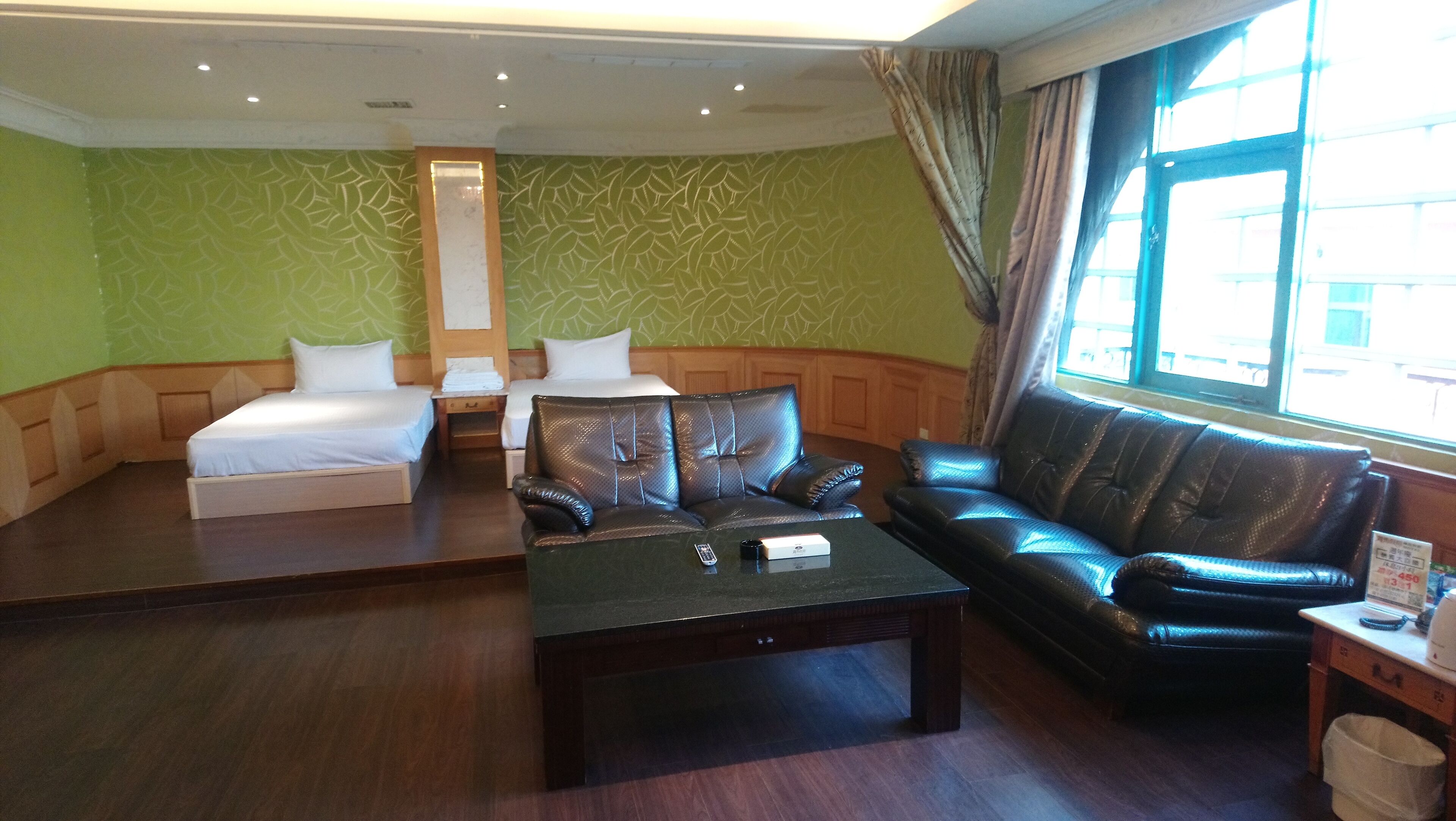 A hotel room with two beds, a leather sofa, a coffee table, and a large window with curtains.
