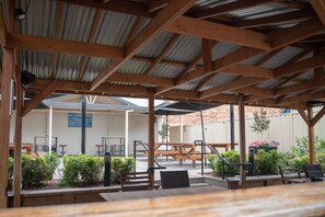 An outdoor patio area with wooden benches and tables, surrounded by plants and a corrugated metal roof. - Castlereagh Hotel (Dubbo)