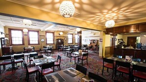Un restaurant spacieux, doté de nombreuses tables et chaises, de grandes fenêtres et d’éléments d’éclairage décoratifs.