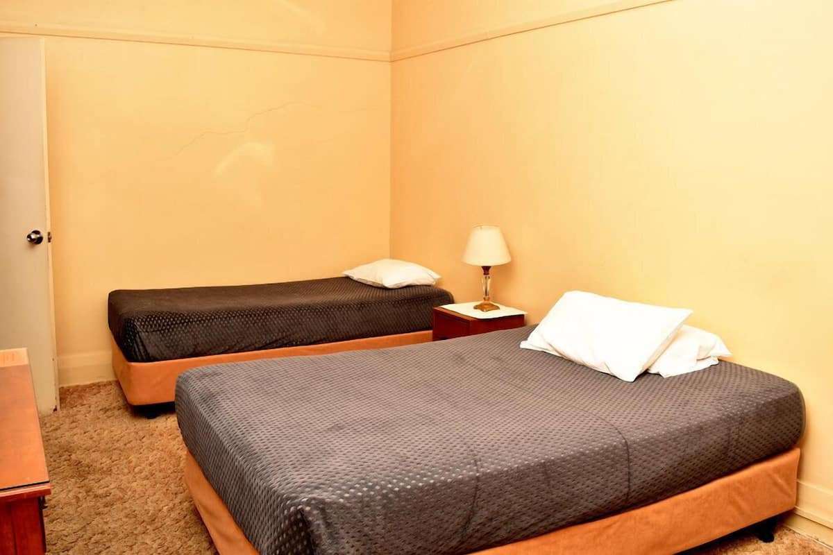 Una habitación de hotel con dos camas, una mesita de noche con una lámpara y una puerta.