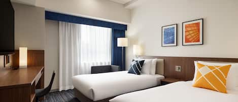 A hotel room with two beds, a desk, a chair, and a large window with curtains.