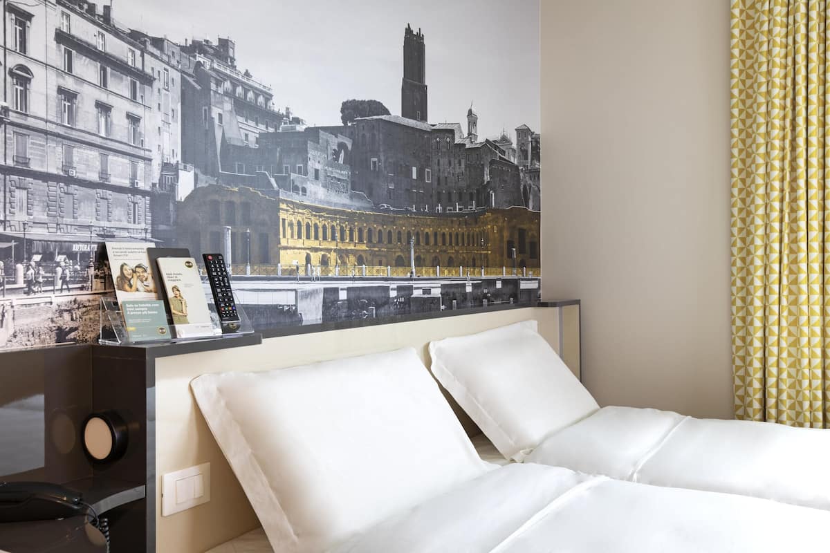 Habitación de hotel con cama, teléfono, fotografía enmarco y una obra de arte en la pared que representa un paisaje urbano.