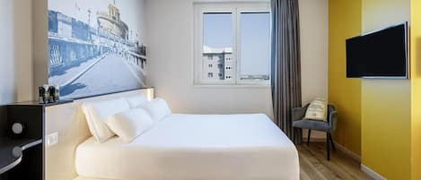 A hotel room with a bed, a desk, a chair, a TV, and a window with curtains.