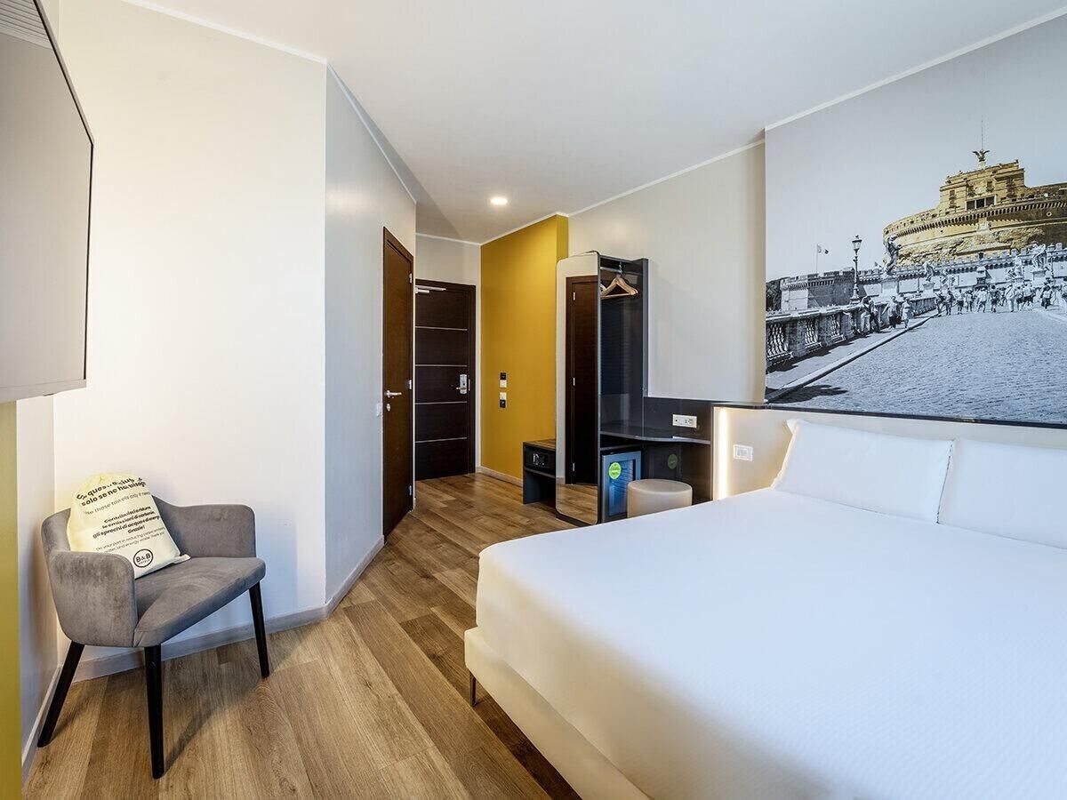 A hotel room with a bed, a chair, a desk, and a wall-mounted TV.
