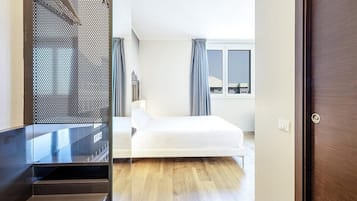 Habitación de hotel con cama, ventana con cortinas, puerta y vista a la ciudad.