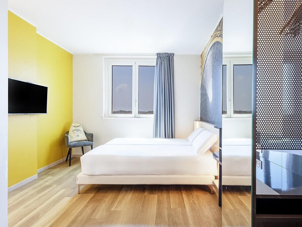 Una habitación de hotel con una cama, un escritorio, una silla, un televisor y una ventana con cortinas.
