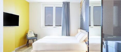 Una habitación de hotel con una cama, un escritorio, una silla, un televisor y una ventana con cortinas.
