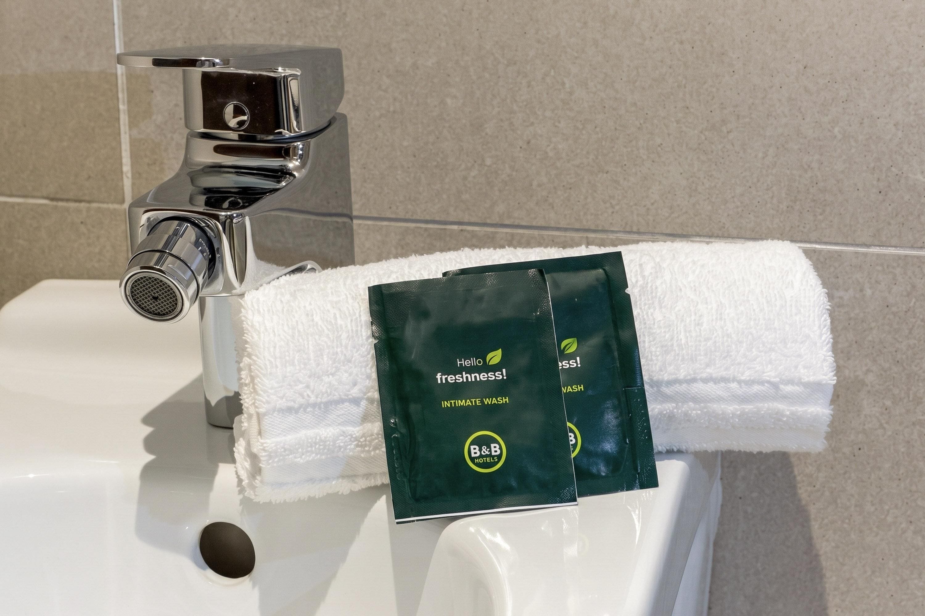 Ein Waschtisch mit Spender für Handtücher, der eine grüne Packung mit der Aufschrift 'Hello Freshness! Intimate Wash' von B&B Hotels enthält.