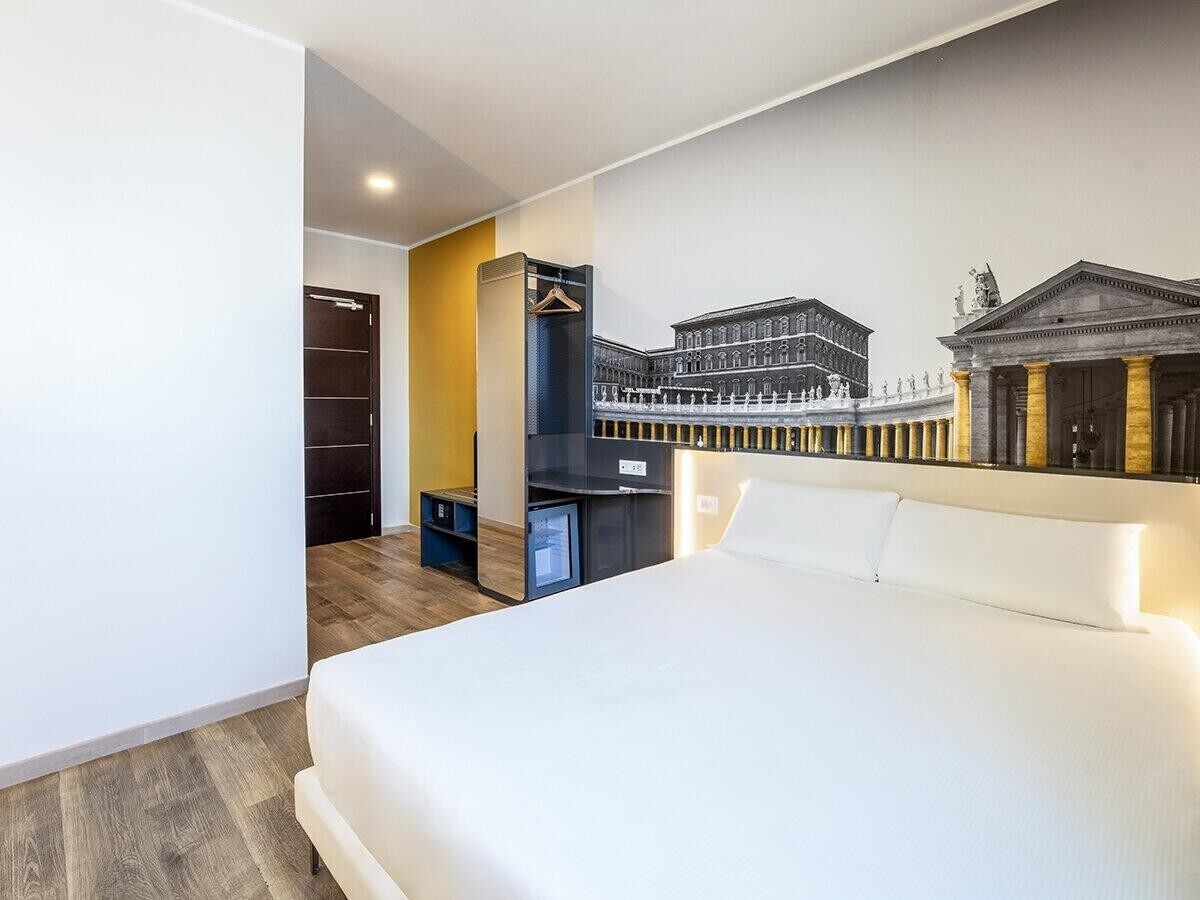 Une chambre d’hôtel avec un grand lit, une armoire, un bureau avec une chaise et un téléviseur fixé au mur.