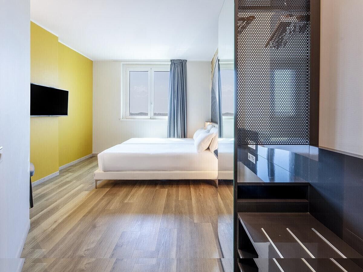 Un dormitorio moderno con cama, ventana con cortinas, televisor montado en la pared y piso de madera.