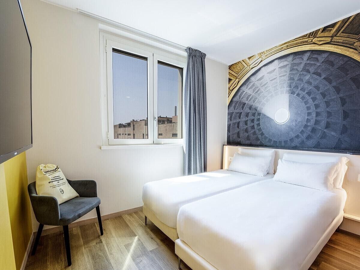 A hotel room with two beds, a window, a chair, and a decorative ceiling.