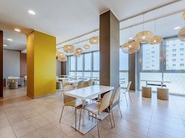 A modern dining area with white tables and chairs, large windows, and hanging wicker lamps.