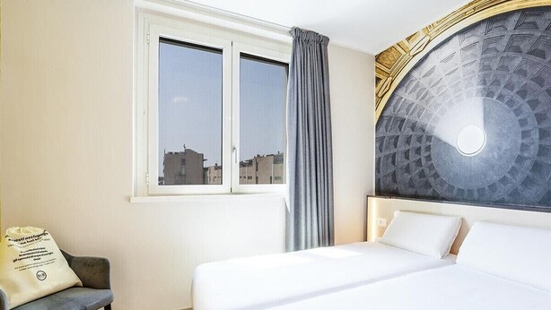 A hotel room with a bed, a chair, a window, and a decorative wall. - B&B Hotel Roma Fiumicino Aeroporto Fiera 1 (Fiumicino)
