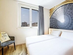 A hotel room with a bed, a chair, a window, and a decorative wall. - B&B Hotel Roma Fiumicino Aeroporto Fiera 1 (Fiumicino)