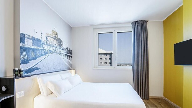 A hotel room with a bed, a window with curtains, a flat-screen TV, and a wall-mounted artwork. - B&B Hotel Roma Fiumicino Aeroporto Fiera 1 (Fiumicino)
