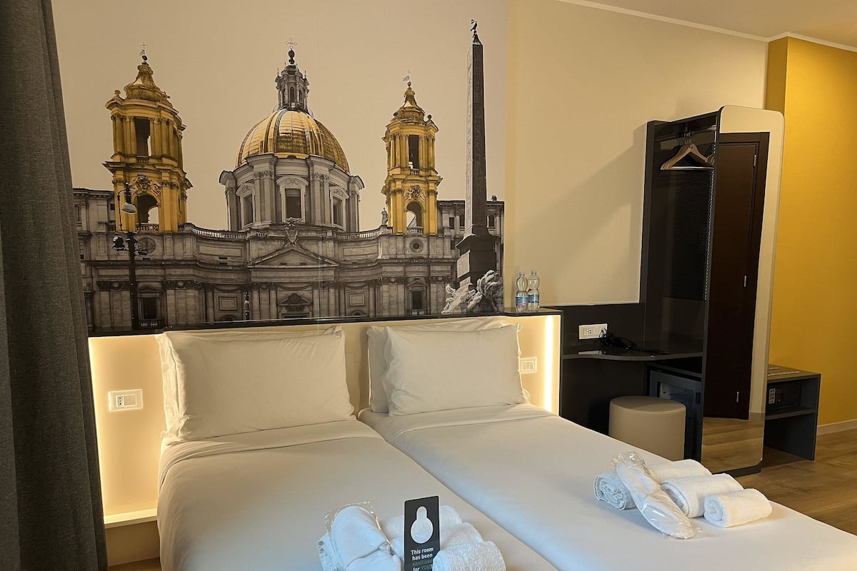 Habitación de hotel con cama, televisor, armario y un mural de un edificio histórico.