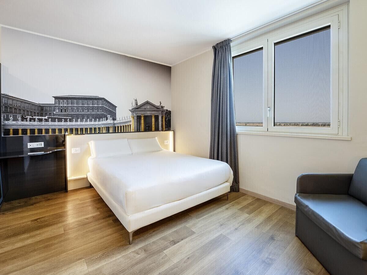 Une chambre d’hôtel avec un lit, un bureau, une chaise et une fenêtre avec des rideaux.