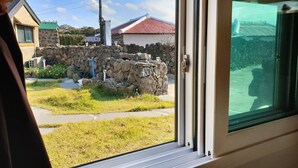 Vista a través de una ventana que muestra un muro de piedra, un espacio con césped y un edificio con techo rojo.