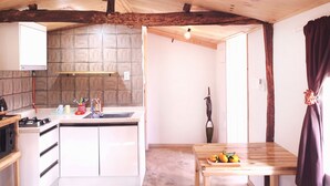 Cocina con armarios blancos, estufa y pileta. Hay una mesa de madera con un frutero.