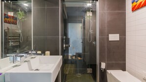 Un baño moderno con ducha de vidrio, un lavamanos blanco y un inodoro.