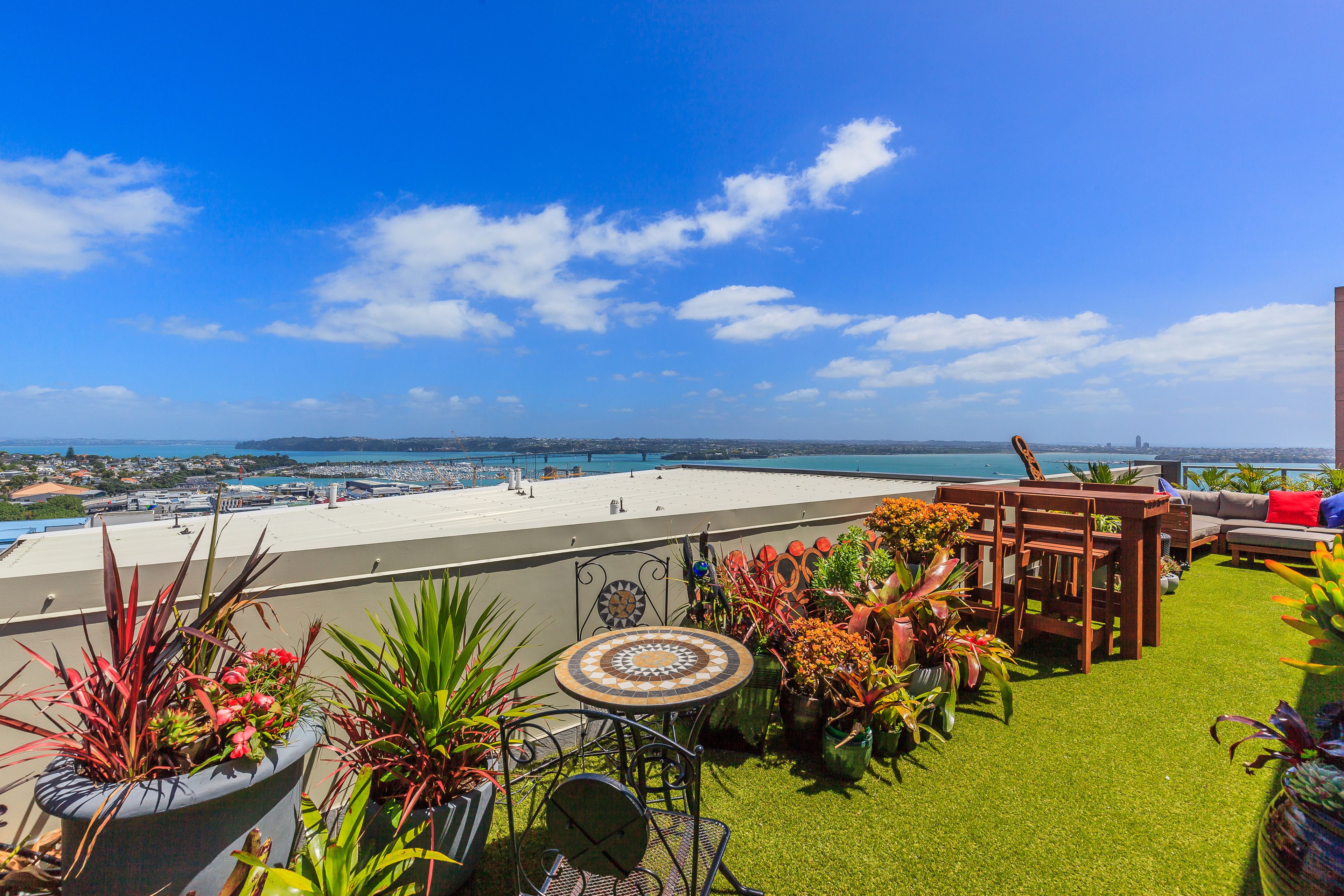 A rooftop terrace with a view of the sea, featuring a dining area, seating, and potted plants.