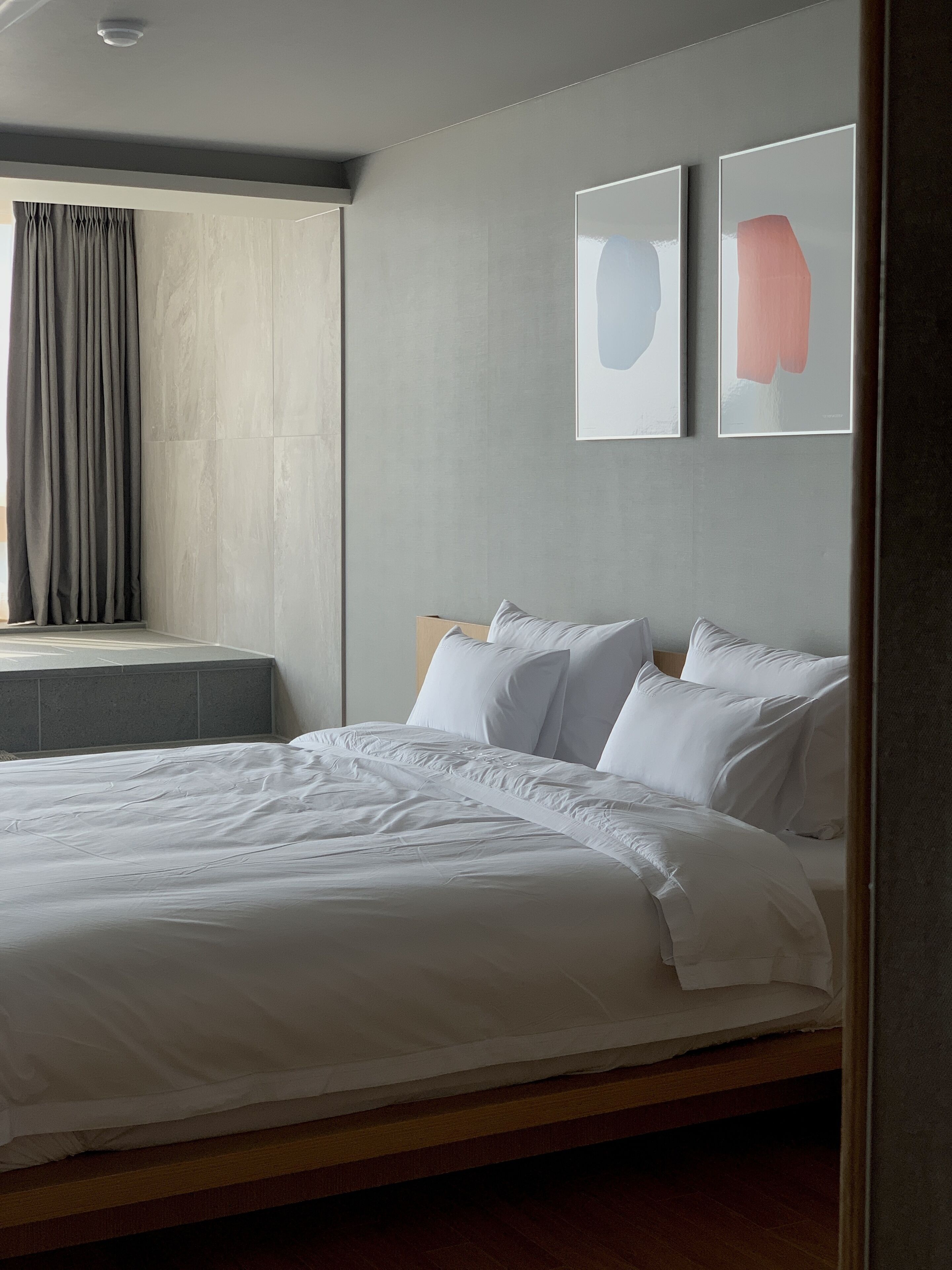 Un dormitorio moderno con una cama grande, una ventana con cortinas y dos obras de arte enmarcadas en la pared.