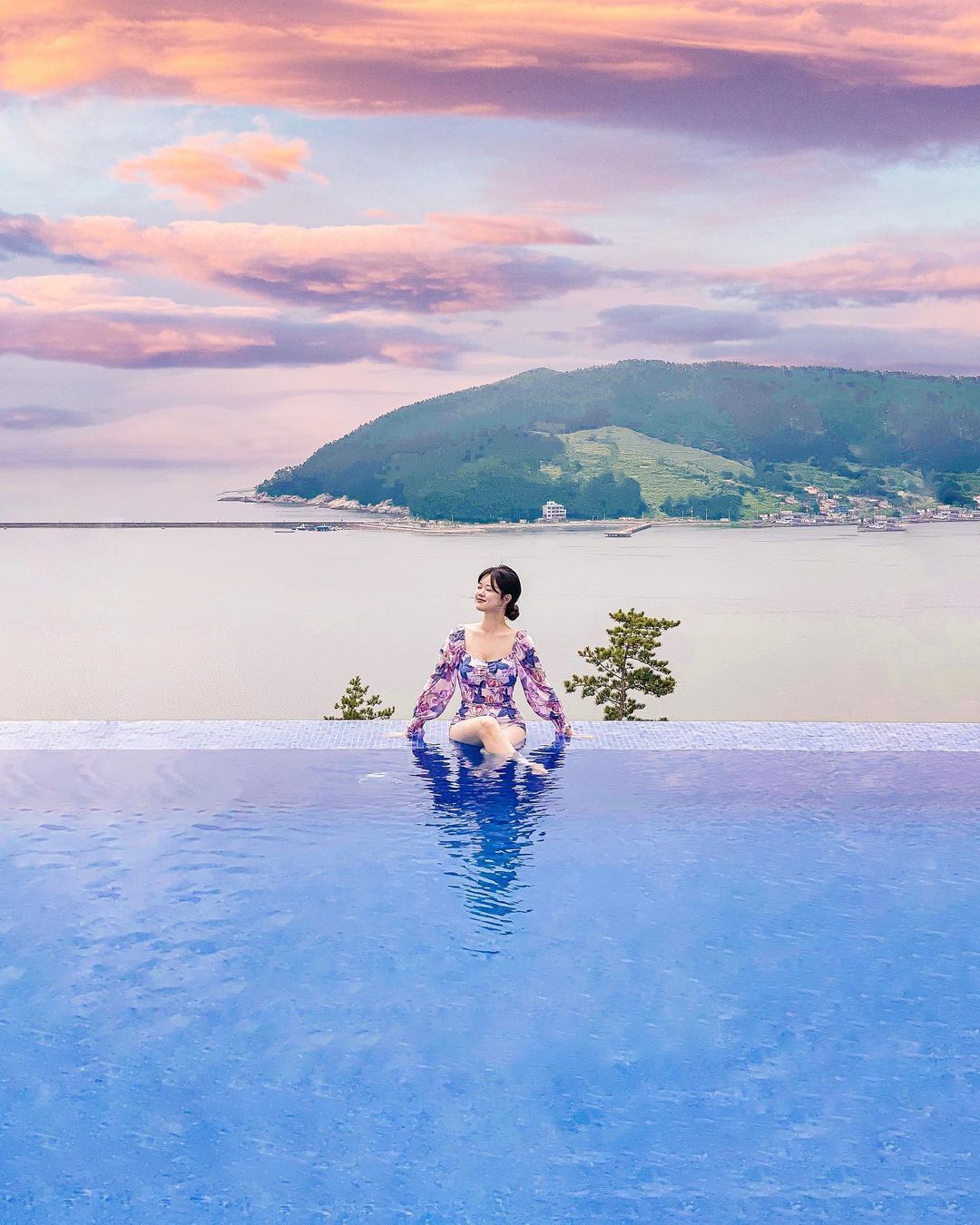 Una persona sentada en una piscina con vistas a una costa lejana y colinas.