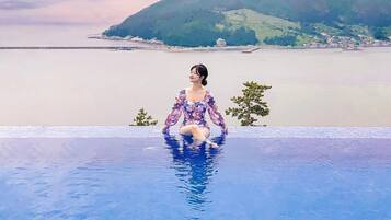 Una persona sentada en una piscina con vistas a una costa lejana y colinas.