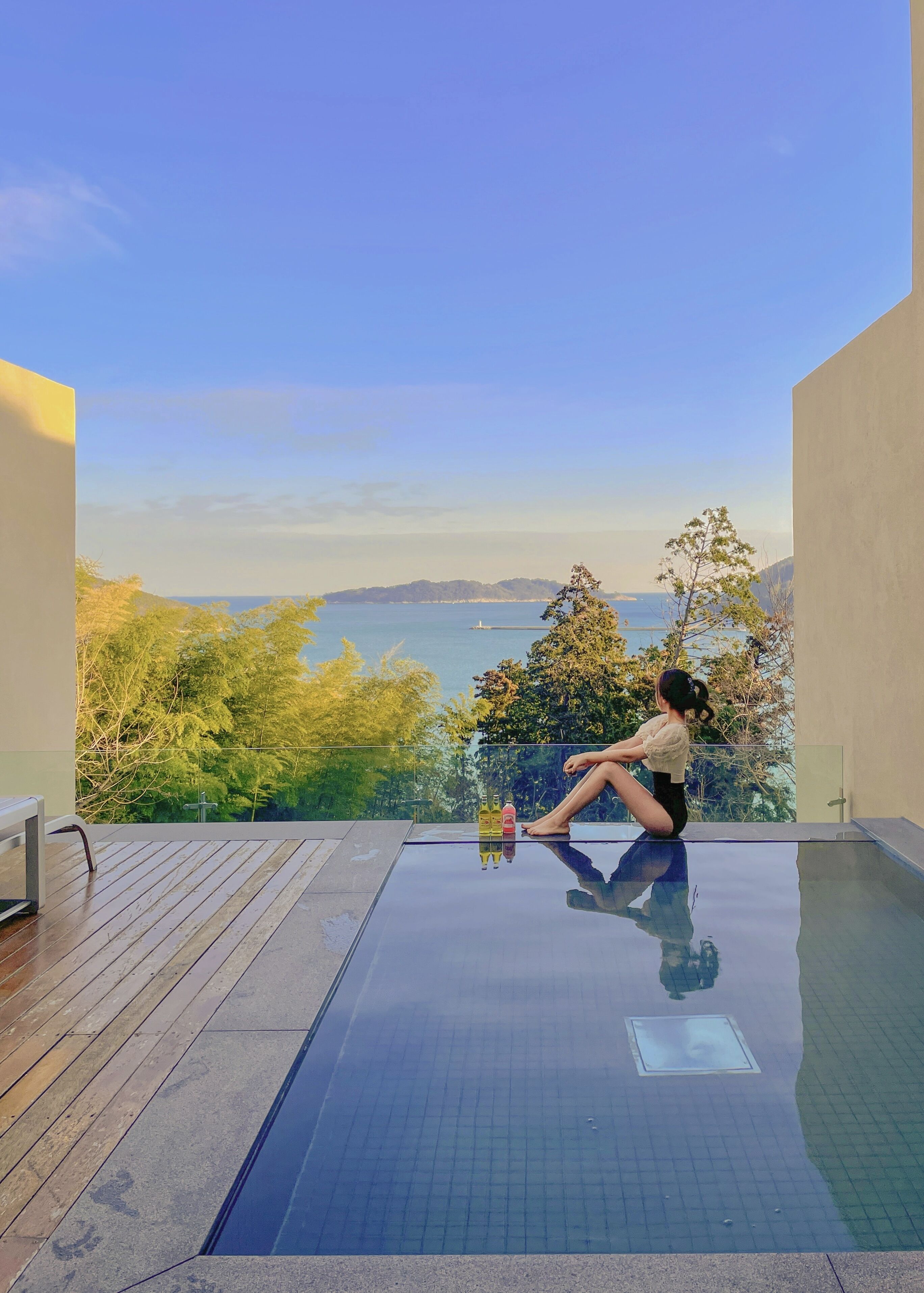 Una persona sentada junto a una piscina con vistas al mar y colinas.