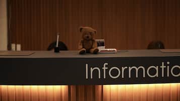 A wooden reception desk with a teddy bear and a pen on it.