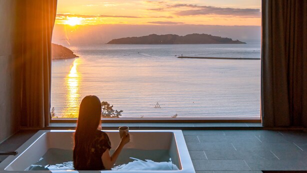 A woman in a bathtub with a view of a sunset over water. - Hotel SangSang & Private SangSang Pool Villa  (Geoje)