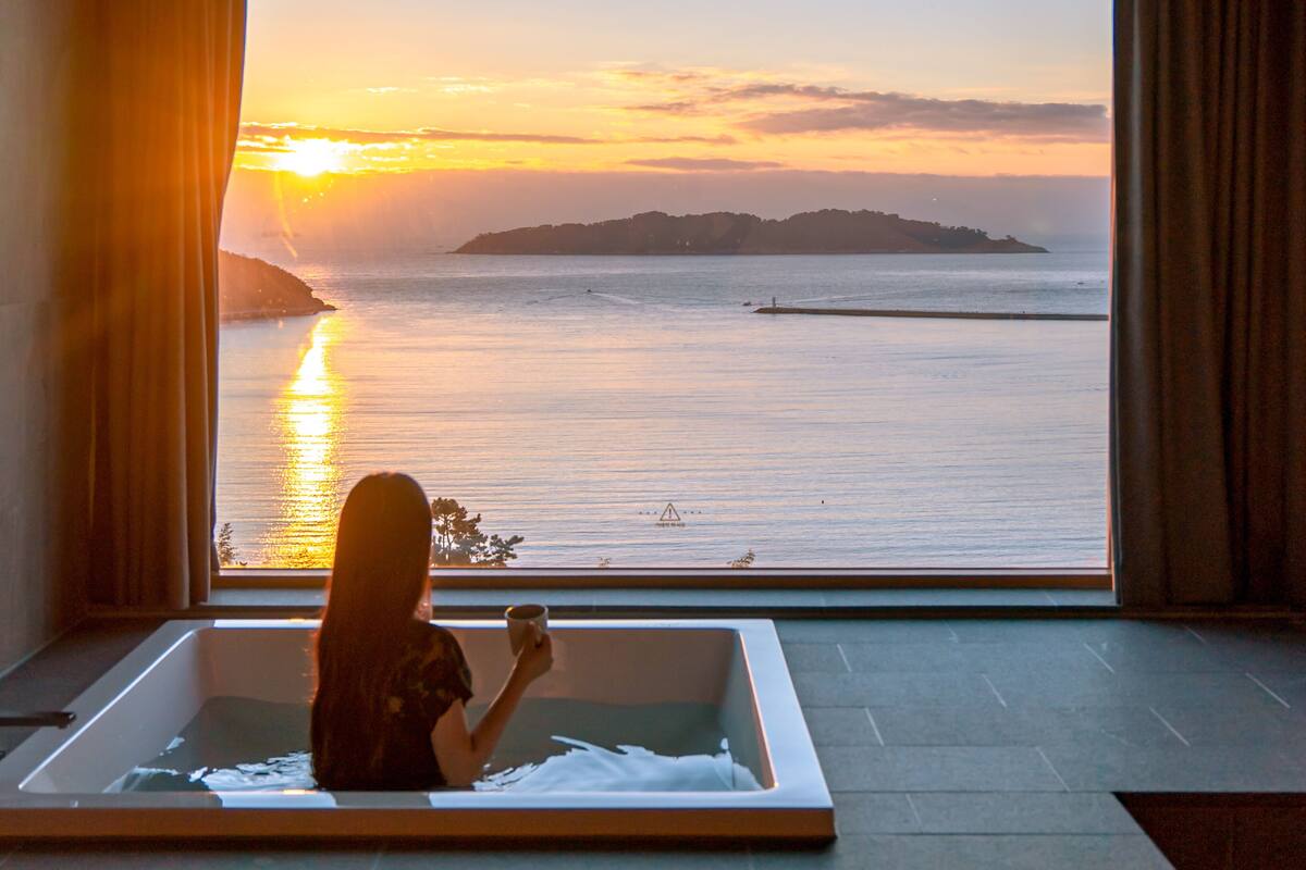 A woman in a bathtub with a view of a sunset over water.