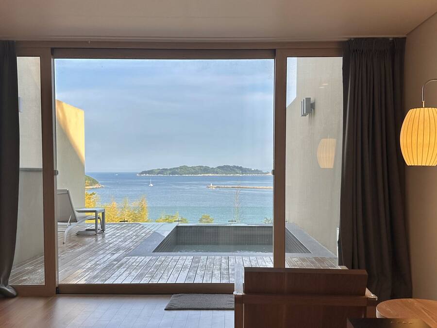 A modern room with a large sliding glass door leading to a balcony with a view of the sea.