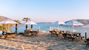 A beachside patio with tables and umbrellas, overlooking a calm sea and distant hills. - Hotel SangSang & Private SangSang Pool Villa  (Geoje)