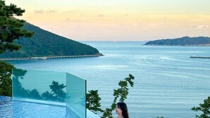 A woman sitting by a clear blue infinity pool with a view of the sea and a distant island. - Hotel SangSang & Private SangSang Pool Villa  (Geoje)