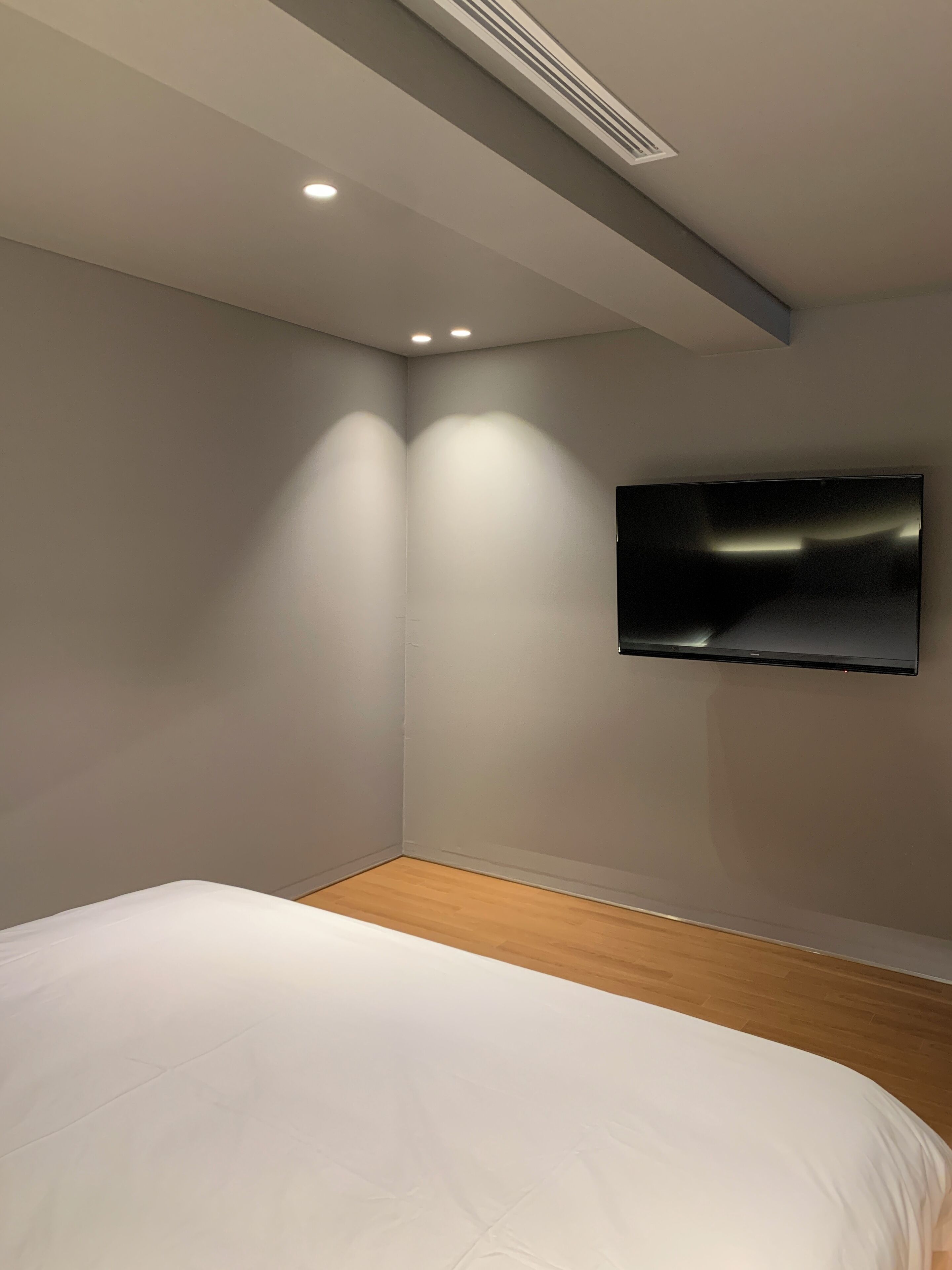 Une chambre moderne avec un grand lit, un téléviseur fixé au mur et un éclairage encastré au plafond.