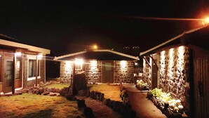 Um edifício de pedra com um pátio coberto, um pequeno jardim e um caminho que leva a uma porta.