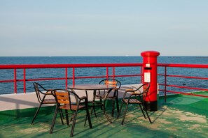 A table and chairs on a deck with a red railing, overlooking a body of water. - Fantastic Ocean View Sydney Hotel (Jeju City)