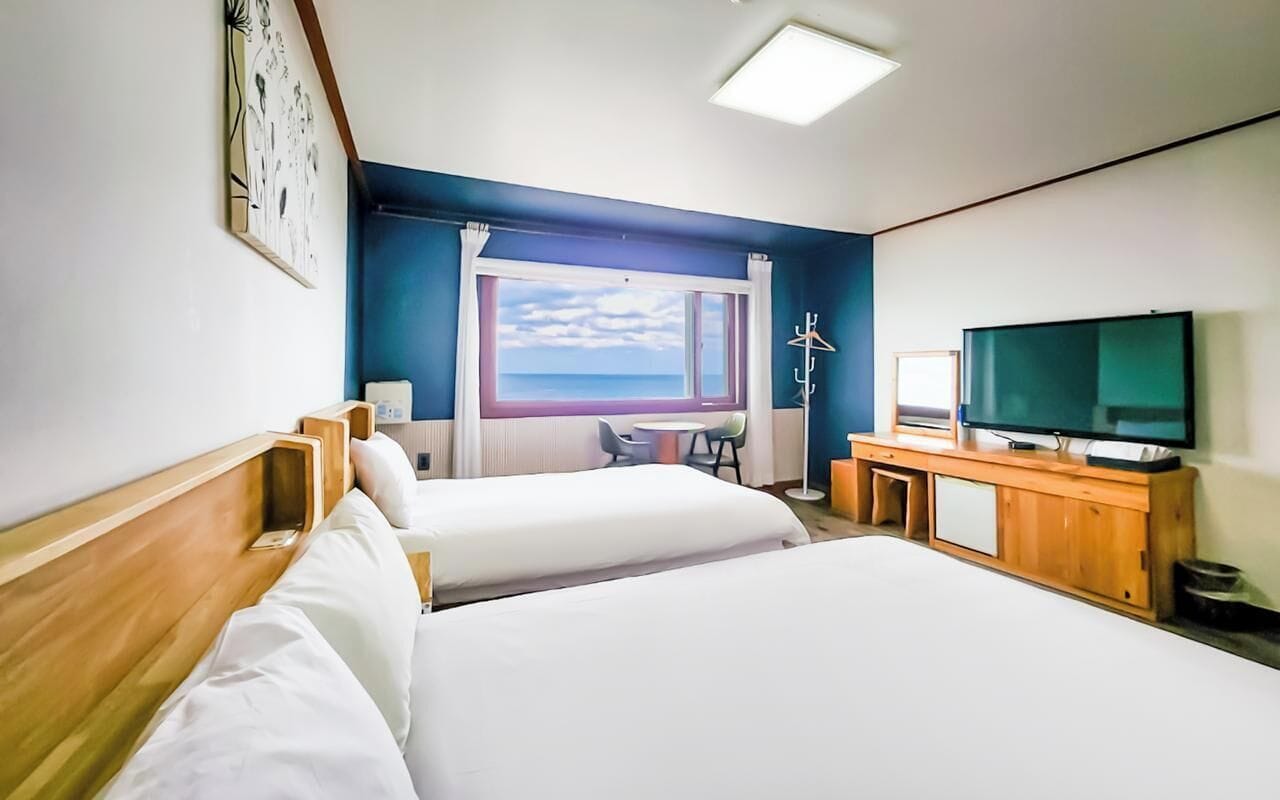 A hotel room with two beds, a television, a desk, and a window with a view.