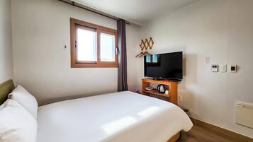 Habitación de hotel con cama, televisor sobre un mueble, ventana con cortinas y un calentador fijado a la pared.