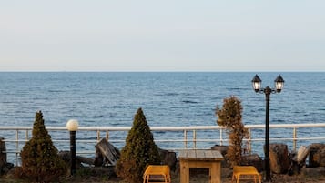 A seaside view with a railing, two chairs, a small table, and two street lamps.