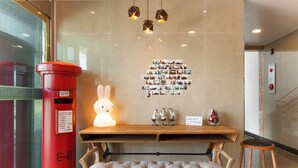 A reception area with a red mail slot, a bulletin board with photos, a wooden bench, and a small stool. - Fantastic Ocean View Sydney Hotel (Jeju City)