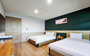 A hotel room with two beds, a wooden desk, a small bedside table, a wall-mounted TV, and a door.